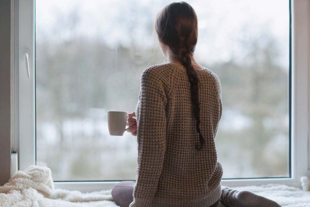 Donna che guarda dalla finestra d'inverno